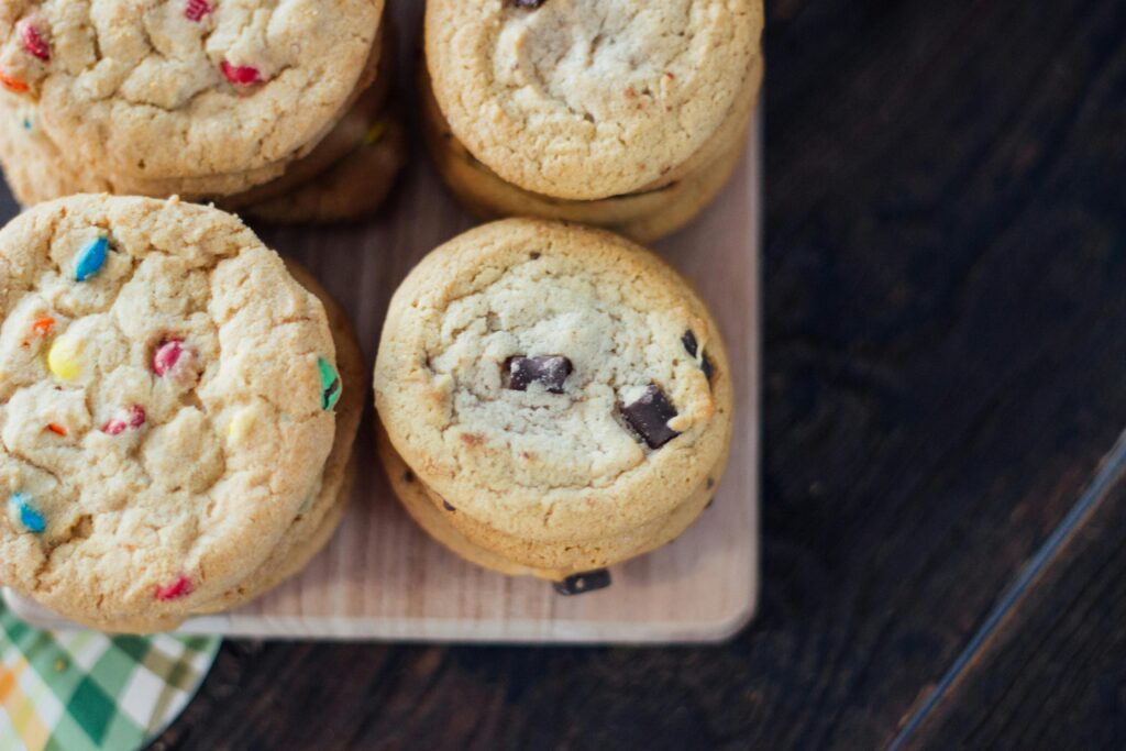 Stack of freshly baked chocolate chip cookies with colorful candies on a wooden board.